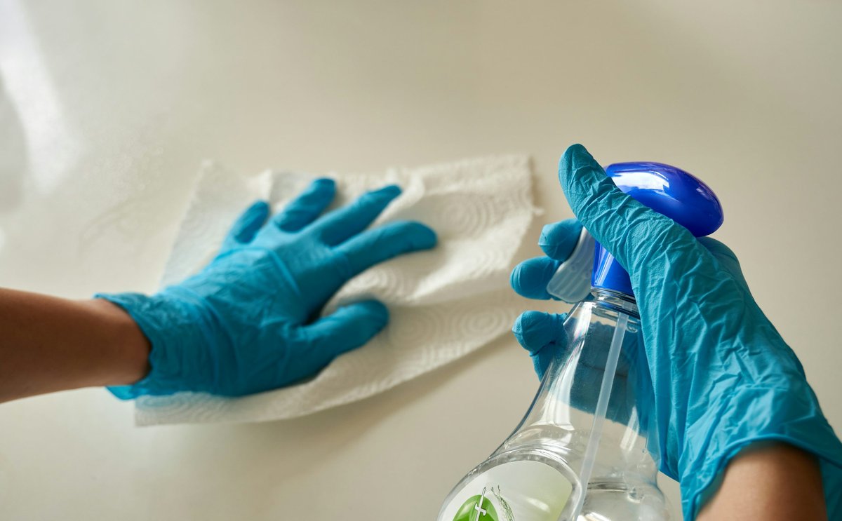 Illustrative photo of gloved hands cleaning a surface with a spray bottle